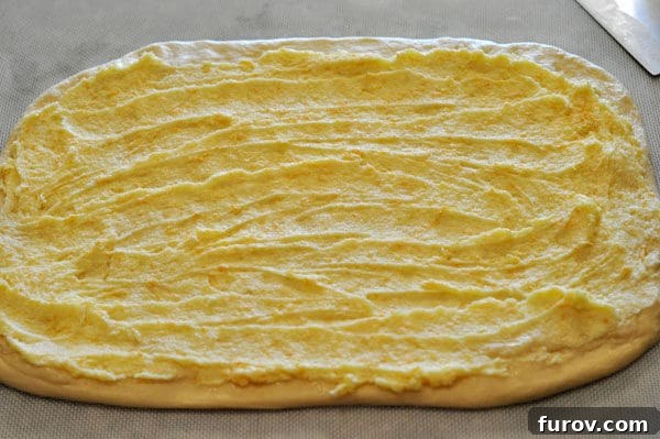 Golden Orange Swirls 6 Rectangle shaped uncooked bread dough with a rich orange zest and butter mixture generously spread across its entire surface.