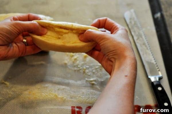 Golden Orange Swirls 9 Hands gently stretching an uncooked sweet roll into an oblong shape, showcasing the rich orange filling within the dough.