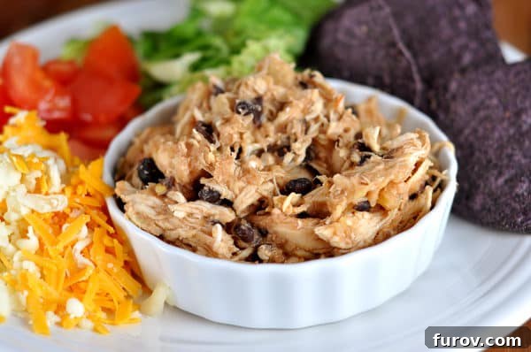 Tropical Slow Cooker Pineapple Salsa Chicken 2 Small white ramekin with shredded chicken and black beans on a plate surrounded with toppings, showcasing the rich colors of the slow cooker pineapple salsa chicken.