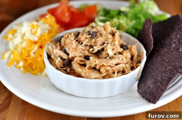 Tropical Slow Cooker Pineapple Salsa Chicken 3 Shredded chicken and black beans in a white ramekin with cheese, tomatoes, lettuce, and chips surrounding it, presenting a delightful serving suggestion.