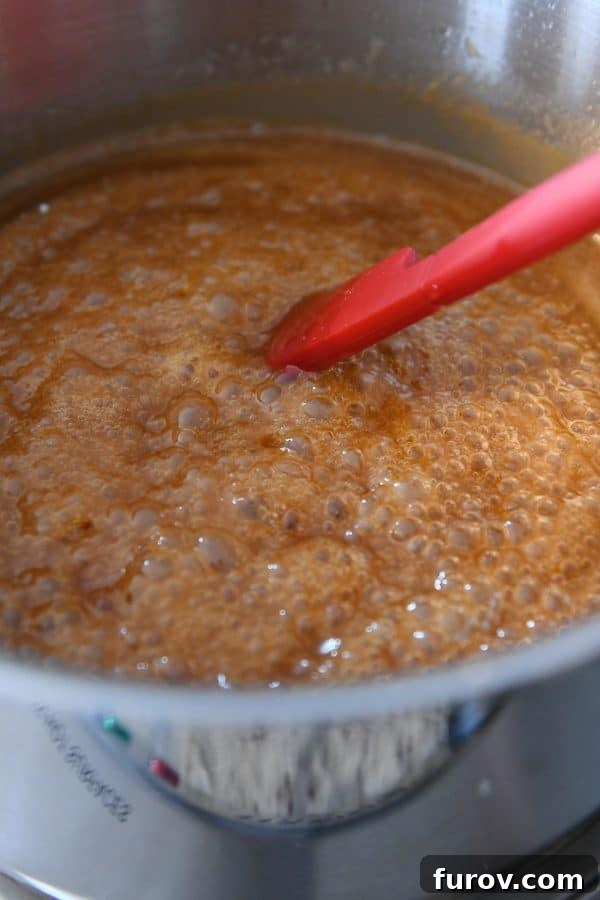 From Scratch Golden Caramel Bliss 12 A spatula stirring the rich, bubbly homemade caramel sauce in a saucepan.