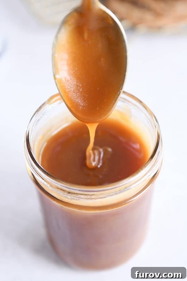 From Scratch Golden Caramel Bliss 15 A spoon skillfully drizzling homemade caramel sauce into a glass jar, highlighting its perfect texture.
