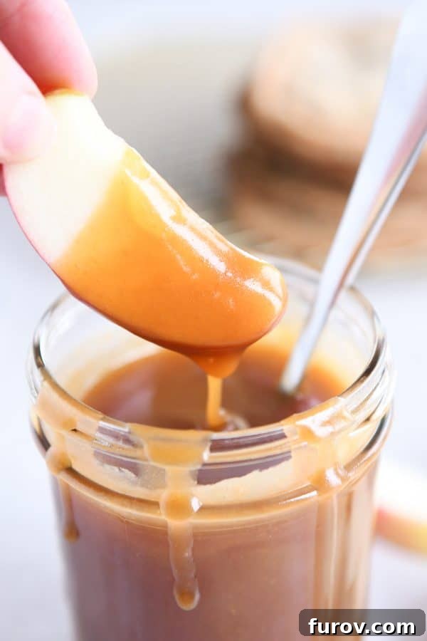 From Scratch Golden Caramel Bliss 4 An apple slice being dipped into a bowl of golden homemade caramel sauce.