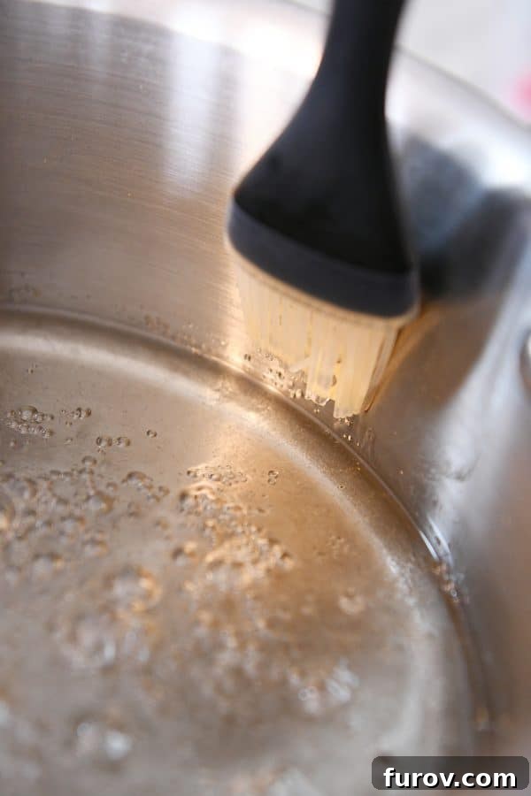 From Scratch Golden Caramel Bliss 7 A wet pastry brush being used to clean sugar crystals from the sides of a saucepan during caramel preparation.