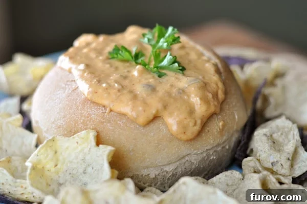 Spicy Chorizo Queso 3 A rustic bread bowl filled with creamy hot chorizo dip, artfully arranged with golden tortilla chips around its base, ready for dipping.