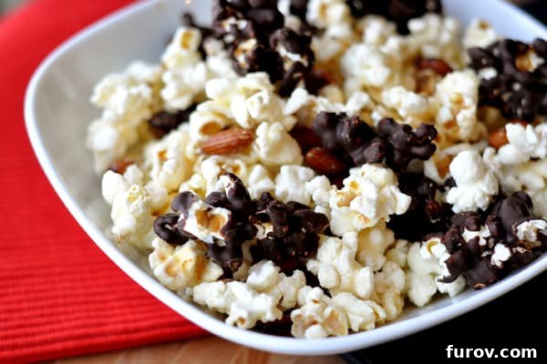 A white bowl full of chocolate-dipped kettle corn, garnished with roasted almonds.