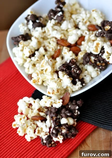 A white dish showcasing a mix of kettle corn, some pieces partially chocolate-dipped, with roasted almonds scattered throughout.