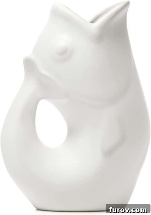 A charming white Gurgle Pot, a fish-shaped pitcher, stands on a countertop, ready to pour and gurgle.