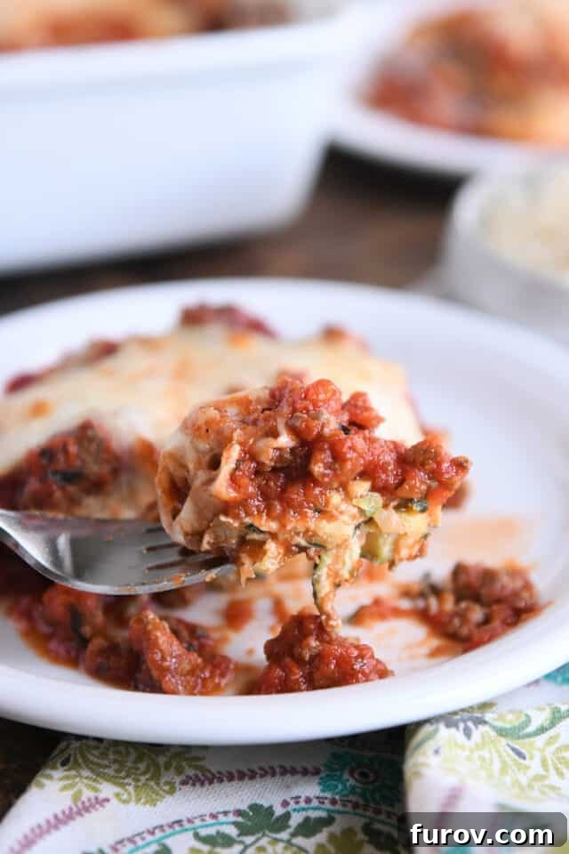 Golden Cheesy Zucchini Spaghetti Bake 7 Fork scooping bite of cheesy zucchini casserole on white plate.