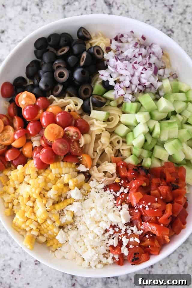 Zesty Mediterranean Pasta Salad 3 Top down view of feta cheese, corn, tomatoes, olives, red onions, cucumbers, red peppers and pasta.