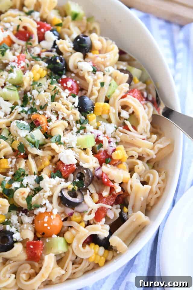 Zesty Mediterranean Pasta Salad 5 Greek pasta salad in large white serving bowl with serving spoon.