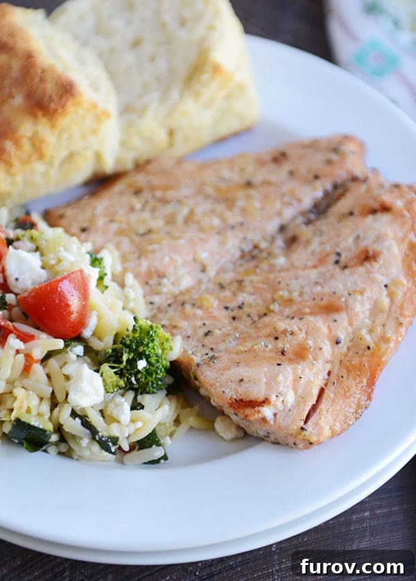 Succulent Grilled Salmon 5 A grilled salmon fillet, biscuit, and helping of pasta salad on a white plate.