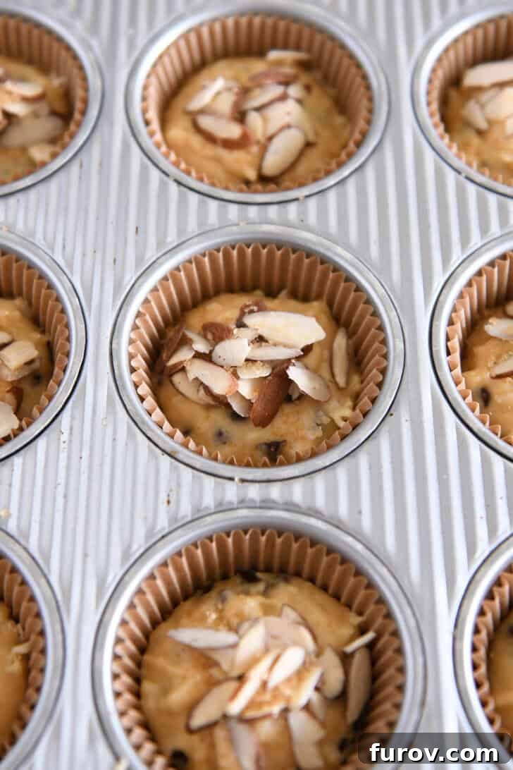 Coconut Almond Bliss Muffins 6 Muffin batter scooped into a lined muffin tin and topped with sliced almonds before baking.