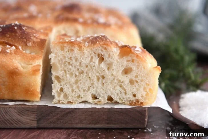 Foolproof No Knead Fluffy Focaccia 3 A square slice of homemade focaccia bread, showcasing its airy, bubbly crumb structure on a piece of parchment paper.