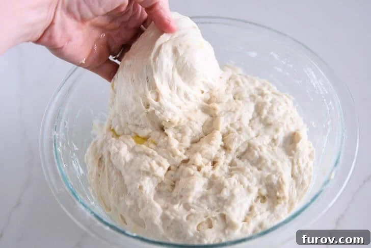 Foolproof No Knead Fluffy Focaccia 6 Performing the stretch and fold technique on the wet focaccia dough in a glass bowl.