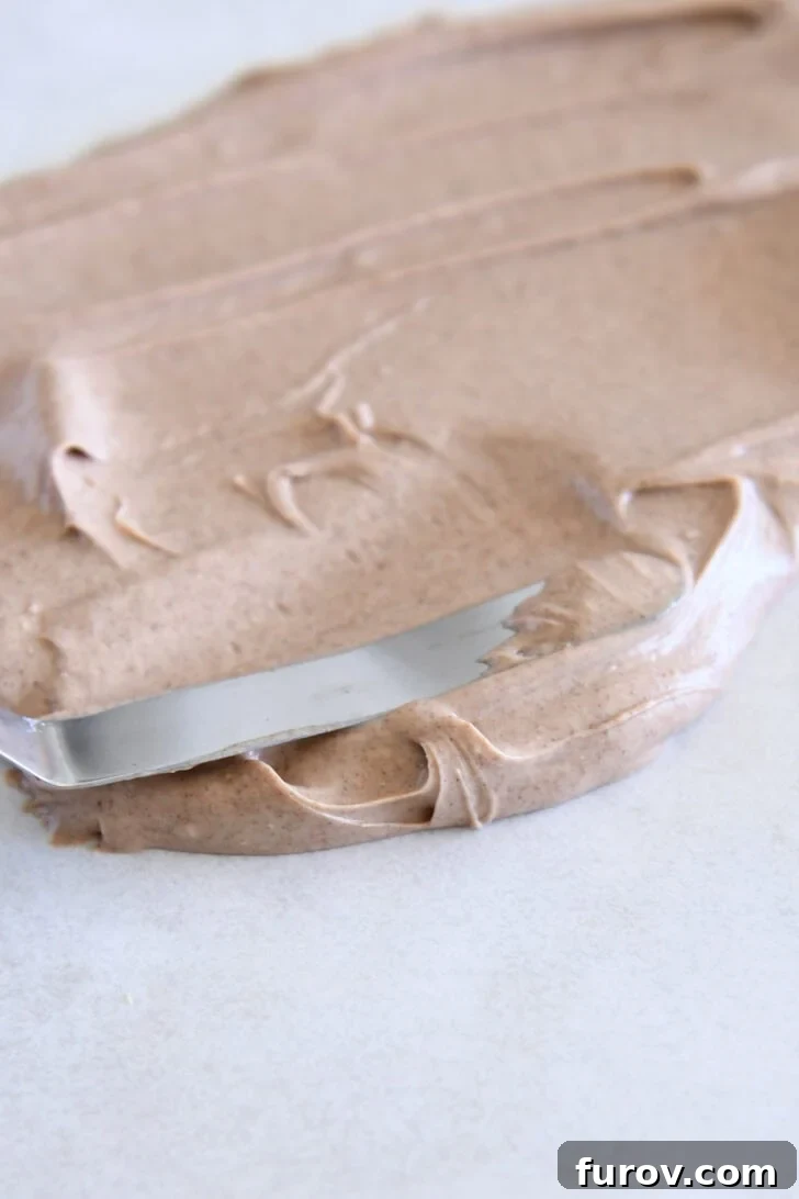 Spreading cinnamon white chocolate mixture on parchment paper with offset spatula.
