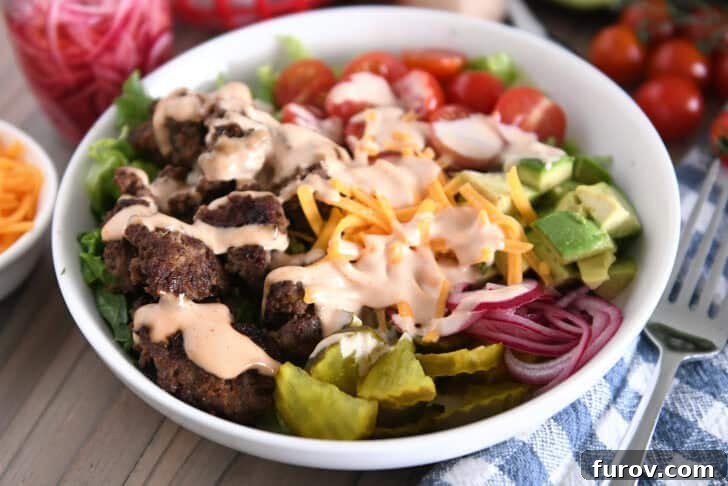 Cooked ground beef, pickles, lettuce, pickled red onions, tomatoes, fries and creamy sauce in white bowl.