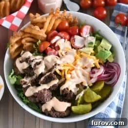 Cooked ground beef, pickles, lettuce, pickled red onions, tomatoes, fries and creamy sauce in white bowl.