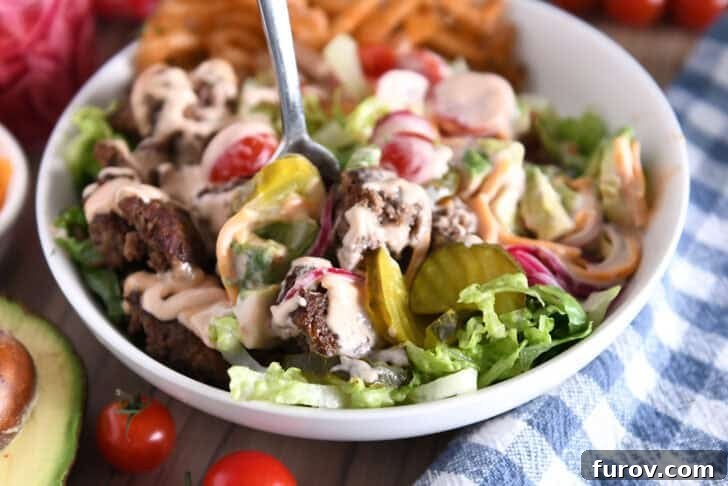 Cooked ground beef, pickles, lettuce, pickled red onions, tomatoes, fries and creamy sauce in white bowl.