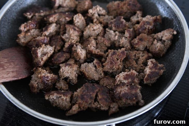 Chunks of crispy ground beef cooking in skillet.