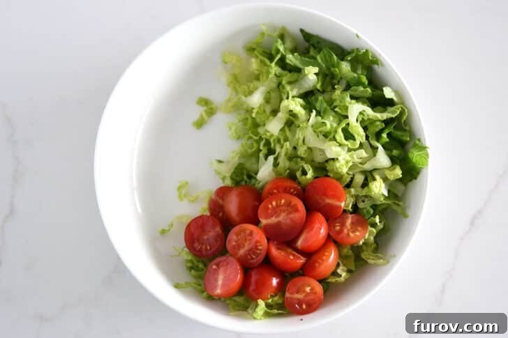 Top down view of lettuce and tomatoes in white bowl.