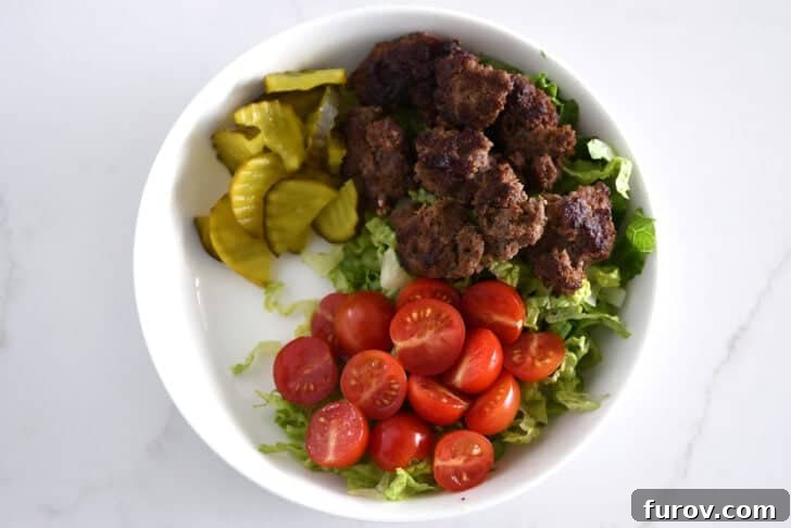 Top down view of lettuce, ground beef, tomatoes, pickles in white bowl.