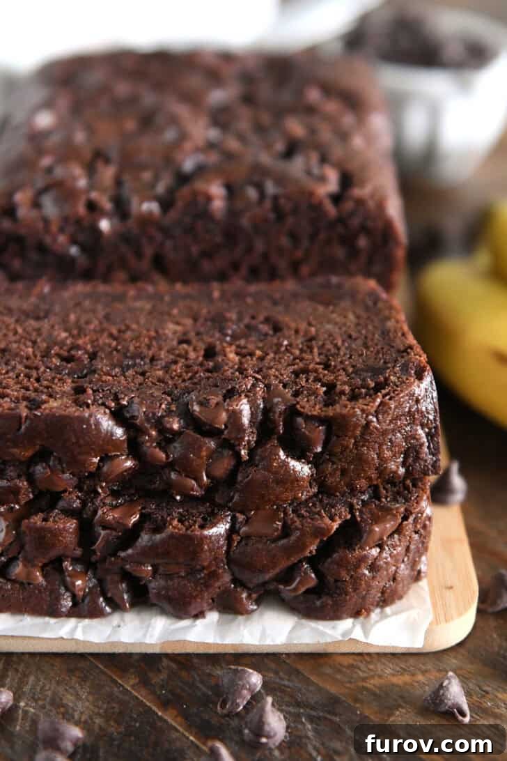 Chocolate Banana Bread with Sour Cream for Moist Loaves 2 Two slices of chocolate banana bread stacked on parchment paper and wood cutting board.