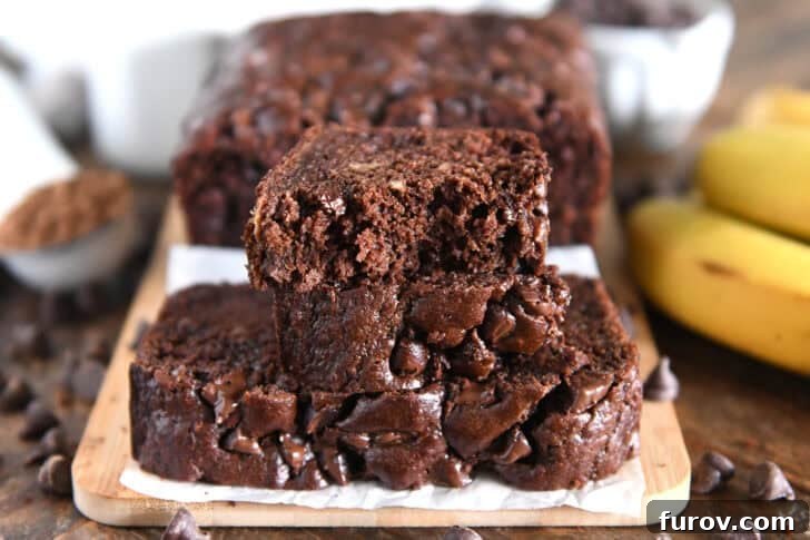 Chocolate Banana Bread with Sour Cream for Moist Loaves 7 Two slices of chocolate banana bread stacked on parchment paper and wood cutting board.