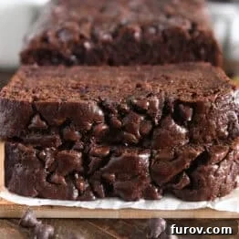 Chocolate Banana Bread with Sour Cream for Moist Loaves 8 Two slices of chocolate banana bread stacked on parchment paper and wood cutting board.
