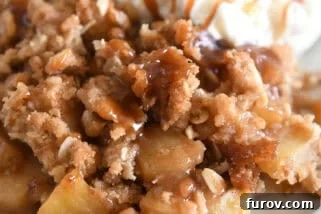 Serving of caramel apple crisp on gray plate with scoop of ice cream.