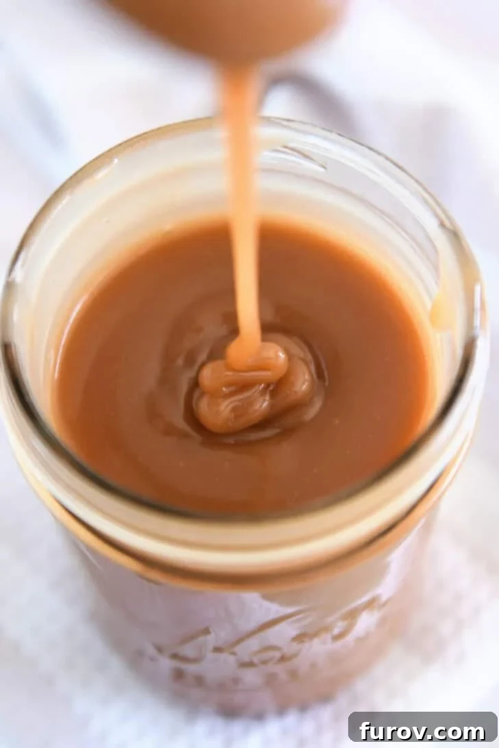 Drizzling caramel sauce from spoon into glass jar.