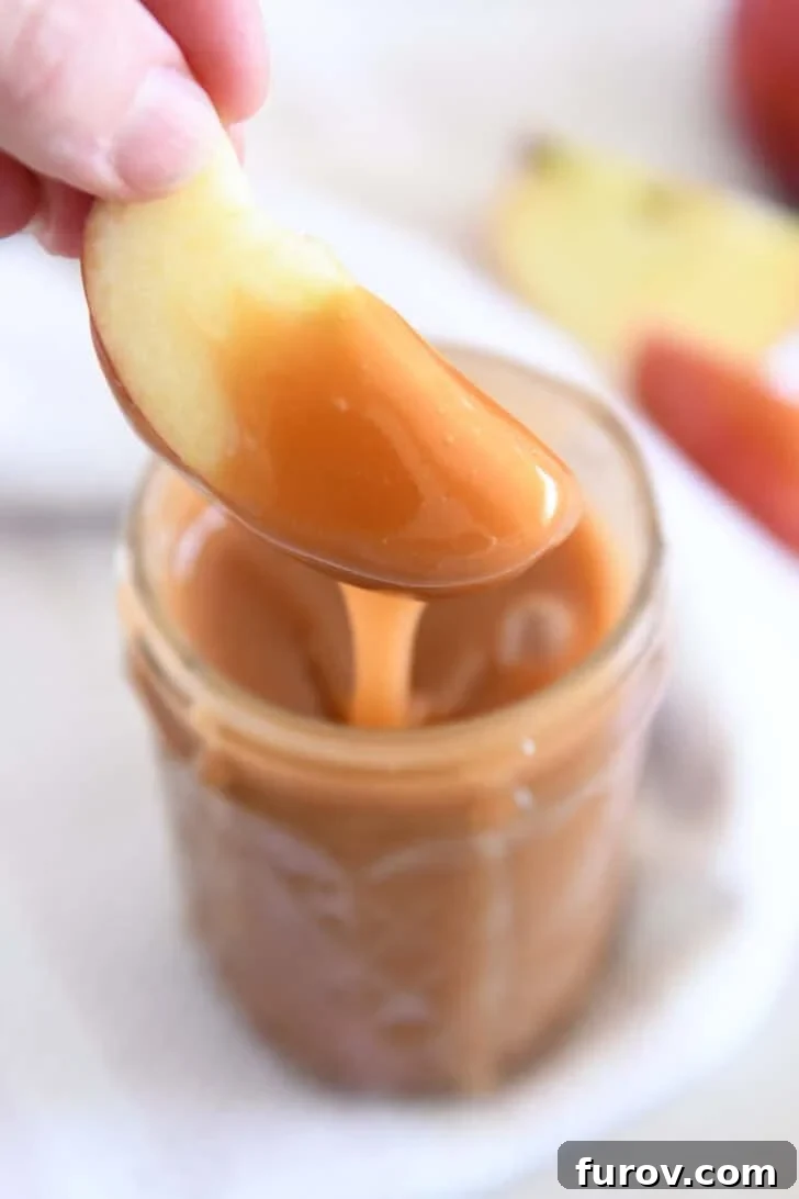 Dipping apple slice into jar of caramel sauce.