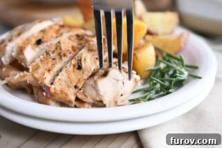 fork taking piece of rosemary ranch chicken on white plate with rosemary and potatoes