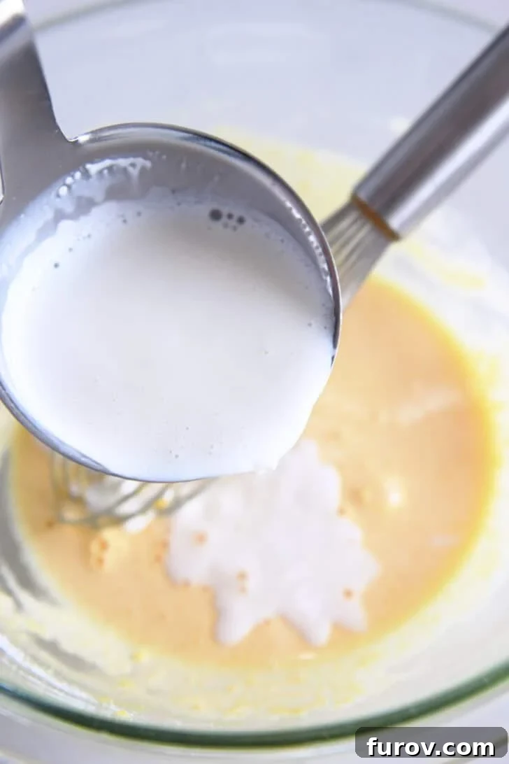 Pouring ladle of hot cream into tempered egg yolks and sugar in glass bowl.
