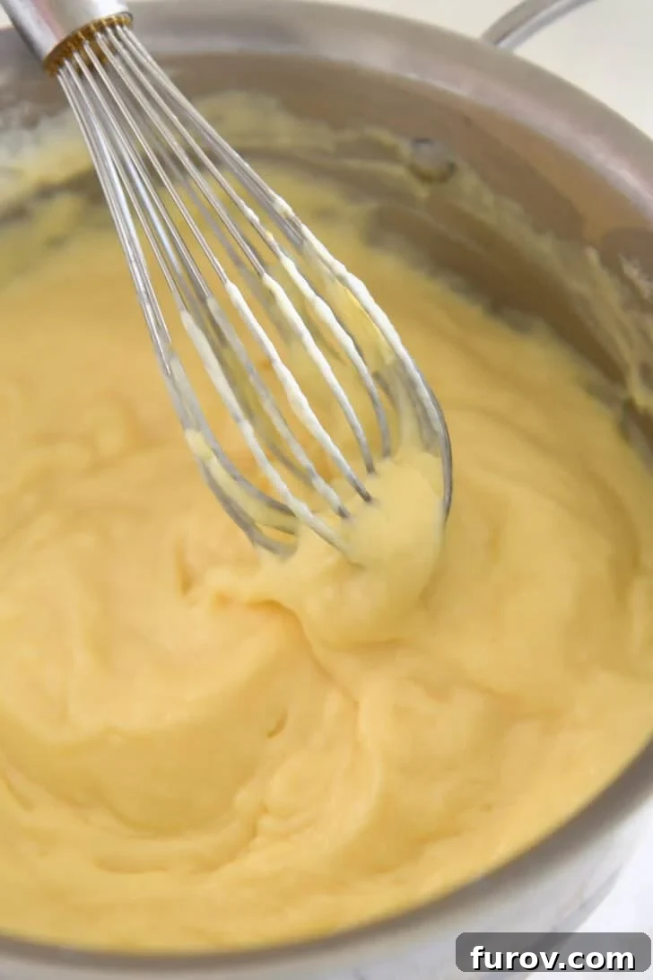 Whisking thick vanilla pudding with wire whisk in stainless pot.