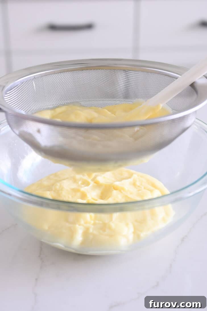 Straining vanilla pudding through fine mesh strainer into glass bowl.