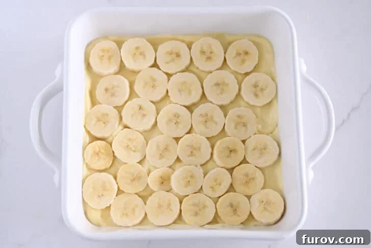 White square 8X8 baking dish with layer of vanilla pudding and sliced bananas.