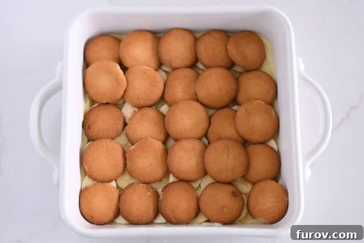 White square 8X8 baking dish with layer of vanilla pudding, sliced bananas, and nilla wafers.