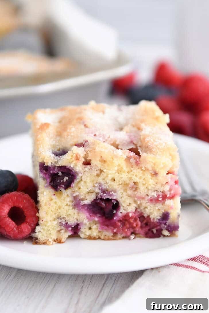 Square of cake with blueberries and raspberries on white plate.