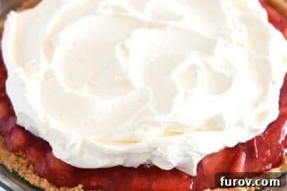 A strawberry pie with graham cracker crust in glass pie plate with whipped cream on top.