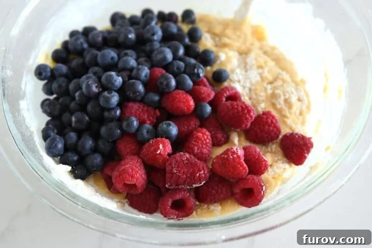 Glass bowl with cake batter, fresh blueberries and fresh raspberries.