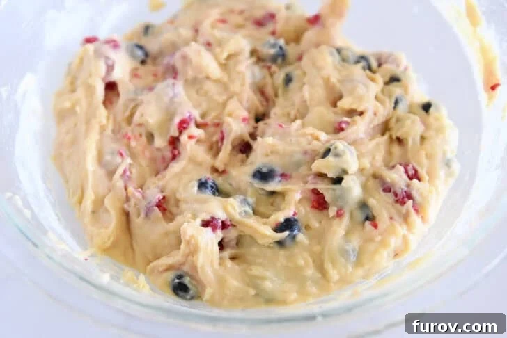 Glass bowl with cake batter with fresh berries mixed in.