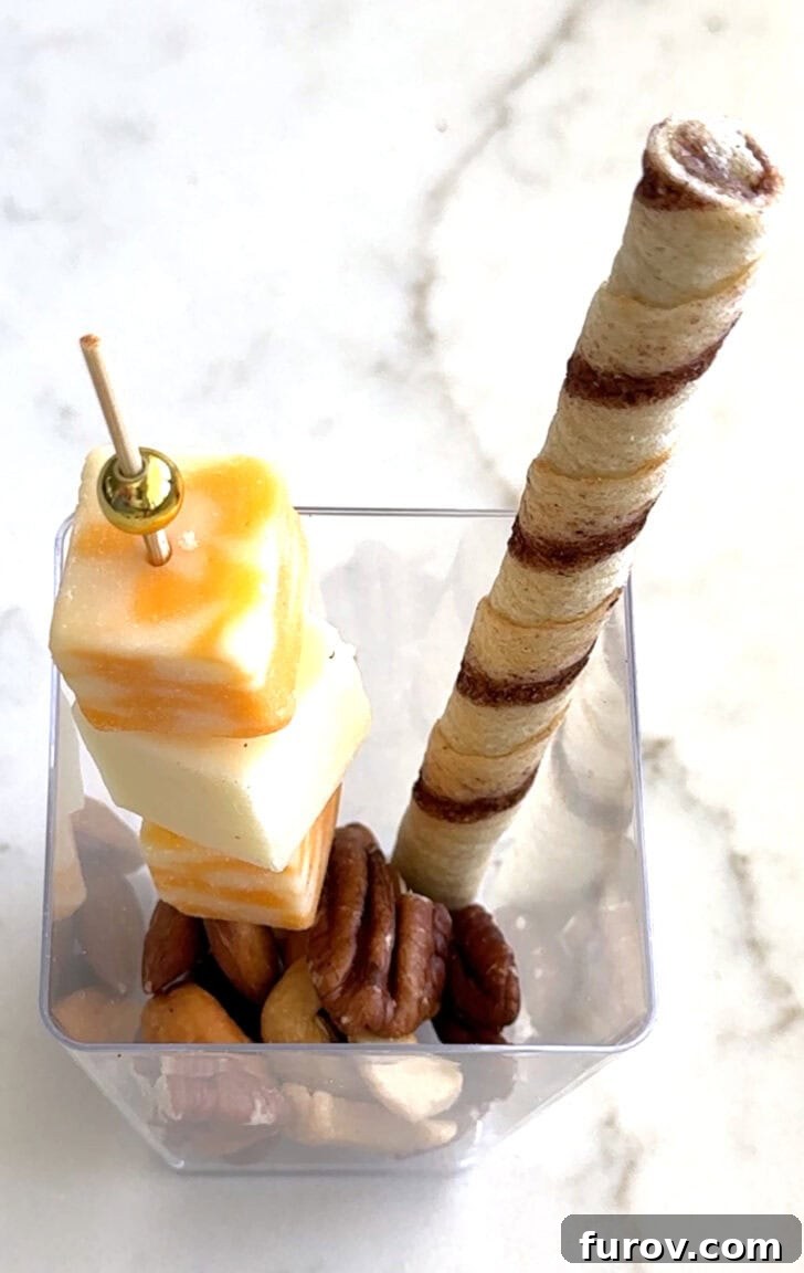 Square plastic cup with cracker, cheese skewer, and pirouline.