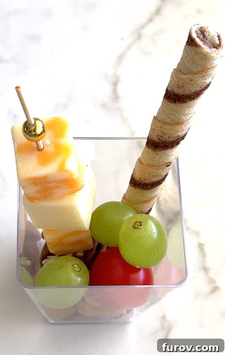 Square plastic cup with cheese skewer, blackberry, and pirouline.