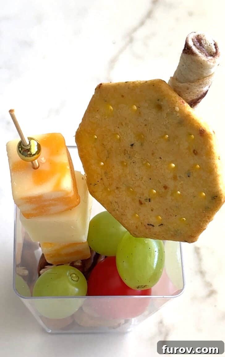 Square plastic cup with cracker, cheese skewer, and pirouline.