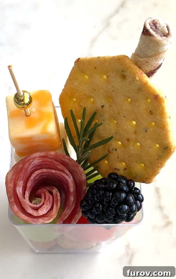 Square plastic cup with cracker, cheese skewer, rolled salami, blackberry, sprig of rosemary and pirouline.
