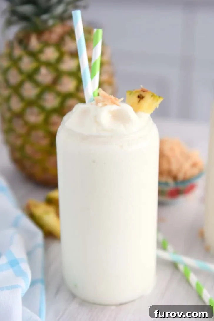 Tall glass cup with frozen piña colada, toasted coconut, a triangle of fresh pineapple and a bit of toasted coconut on top.