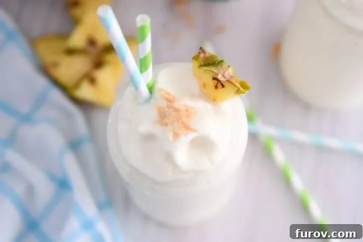Top down view of tall glass cup with frozen piña colada, toasted coconut, a triangle of fresh pineapple and a bit of toasted coconut on top.