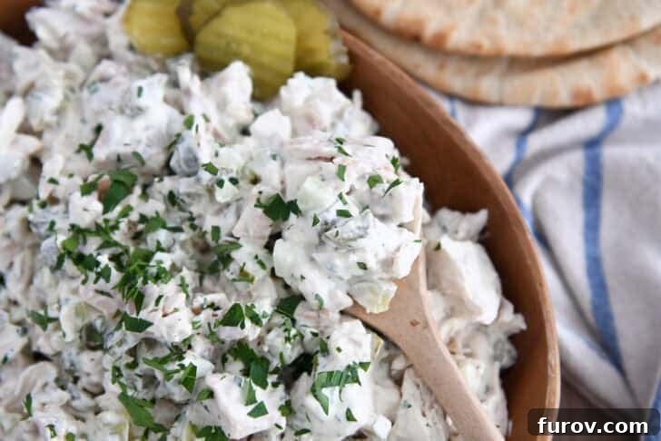Wooden bowl filled with creamy dill pickle chicken salad with wooden spoon.