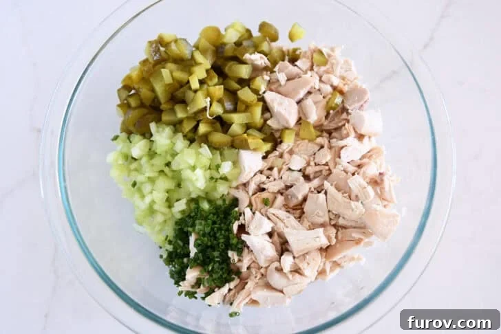 Glass bowl with chopped chicken, chopped green onions, chopped celery, and chopped dill pickles.